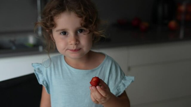 Adorable little girl eating juicy strawberries at home kitchen.Enjoying a snack, healthy healthy dessert from. Vegan nutrition with lots of vitamins for children.