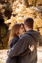 Fototapeta premium Beautiful young couple man and woman hugging in the park near the pond in leaf fall in autumn