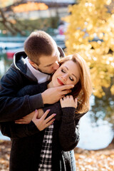 Beautiful young couple man and woman hugging in the park near the pond in leaf fall in autumn
