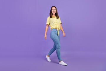 Fototapeta na wymiar Full size photo of nice young brunette lady go wear yellow top jeans shoes isolated on purple color background
