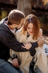 Beautiful young couple man and woman sit on a bench, drink a hot drink from a thermos bottle and hug in a park in a leaf fall in autumn