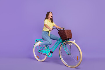 Full body profile photo of cool millennial brunette lady ride bicycle yell wear yellow top jeans sneakers isolated on violet color background