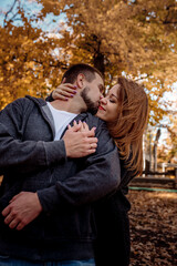Fototapeta premium Beautiful young couple man and woman hugging in the park near the pond in leaf fall in autumn