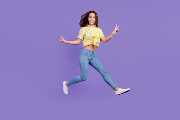 Fototapeta na wymiar Full length photo of cool millennial brunette lady run show v-sign wear yellow top jeans footwear isolated on violet color background