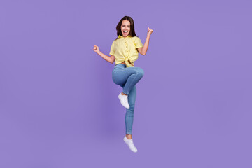 Fototapeta na wymiar Full length photo of celebrate millennial brunette lady jump wear yellow top jeans sneakers isolated on violet color background