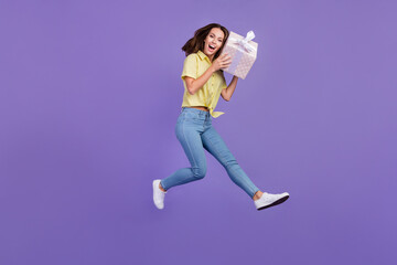 Fototapeta na wymiar Full length photo of impressed millennial brunette lady jump hold present wear yellow top jeans sneakers isolated on violet color background