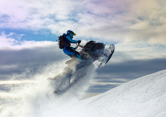 snowmobiler jumps in a bright helmet and overalls over a mountain valley after a snowfall on a...