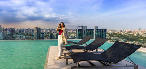 Luxury Asian CEO woman entrepreneur standing on the rooftop swimming pool looking to the sun with...