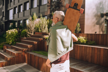 Gray-headed man with the skateboard standing near an office building