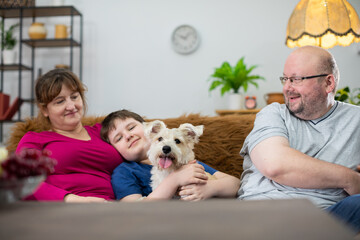 The whole family and their dog are sitting on the sofa in the living room and the dog is looking...