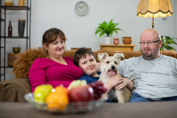 The whole family and their dog are sitting on the sofa in the living room and the dog is looking...