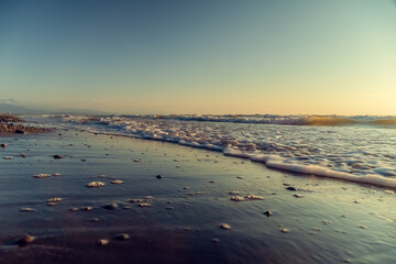 Close-up of sand and small pebbles on the beach against the background of the sea and the sky at sunset. Beautiful nature background