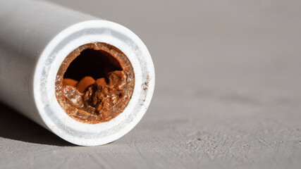 Old broken sludge plumbing polypropylene pipe with red rust and limescale on concrete background...
