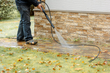 Man cleaning street with high pressure power washer, washing stone garden paths