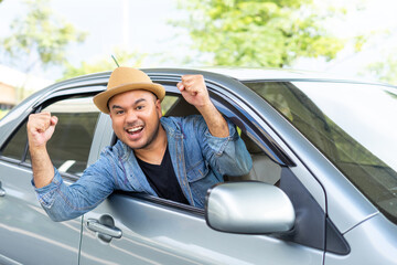 Happy male driver smiling while sitting in a car with open front window. Young asian man smile and looking through window enjoying trip. Man driving his car to travel on his holiday vacation time.