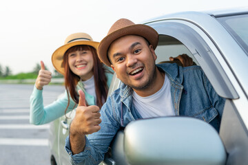 Happy two young friends driver smiling while sitting in a car. Asian man and woman showing thump up and chreeful through window. Young couple wear hats driving car to travel on holiday vacation time.