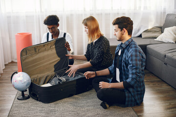 Two men and woman packing the suitcase for a trip