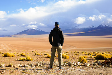 Man looking over the Siloli Desert and its snow topped volcanoes of the Andes from the back of...