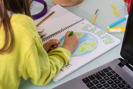 Child girl draws planet earth with wax colors on school notebook for Earth day - Little activist writes the message Save the Planet - Childhood, protection of environment and global warming concept