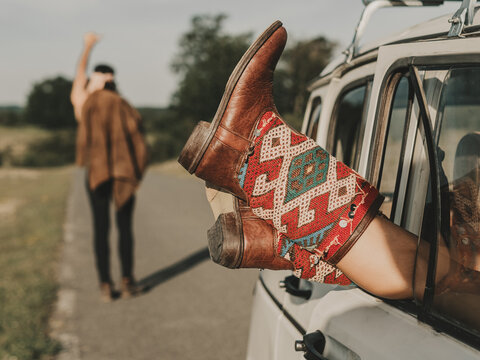 Unrecognizable woman in hippie boots lying in retro car near faceless man