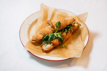 Croissant with salmon and arugula, garnished with herbs and ground pepper. The concept of a delicious hearty homemade breakfast served in a restaurant.