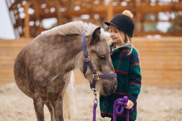 Little girl in hat at ranch with pony