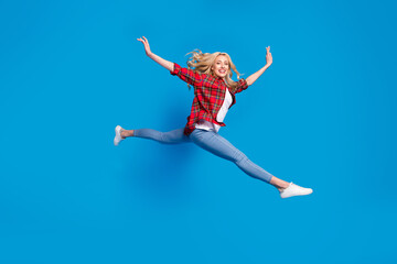 Fototapeta na wymiar Photo of pretty adorable young lady wear plaid shirt smiling jumping high legs hands arms sides isolated blue color background