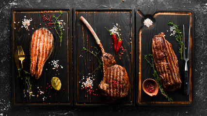 Grill menu. Meat and fish. Set of grilled juicy steaks on a black background, top view