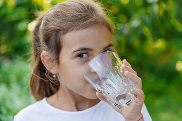 The child drinks water from a glass. Selective focus.
