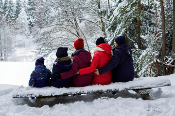 big family, parents and three children are sitting on a bench in a snowy forest bench - Powered by Adobe