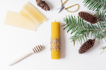 DIY natural beeswax candle for Christmas. Candle, fir branch, pine cones and scissors - obrazy, fototapety, plakaty