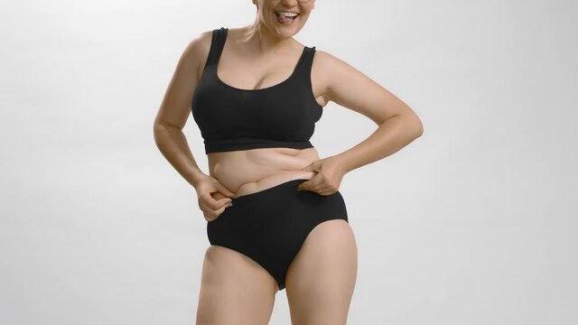 Obese female in black underwear squeezing her belly, laughing and having fun moving. Body positive. Still shot studio video.