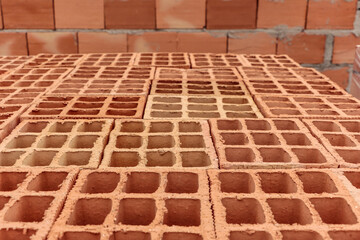 Pile of clay bricks used for building masonry house. In the image, the bricks are laid out, showing their holes, and in the background an already built wall.
