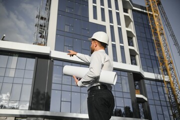 Successful engineer or architect, crane and building construction at backgrpound. Joyous businessman wearing helmet