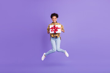 Full size photo of young afro girl happy positive smile hold present box jump party isolated over purple color background