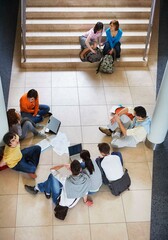 Overhead view of university students sitting on staircase with laptop and papers