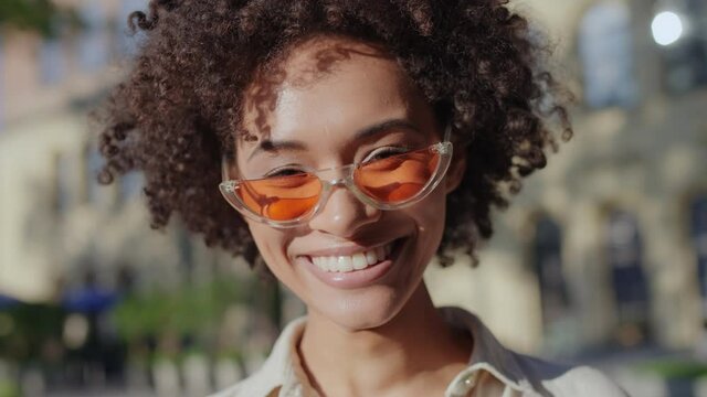 Excited woman with curly hair wearing orange sunglasses and smiling on camera