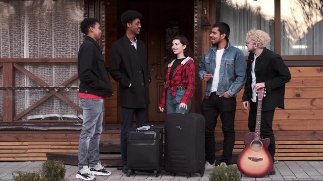 Group frinends with suitcases standing at wooden building