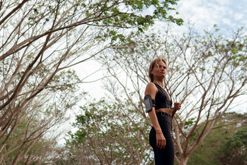 Beautiful woman in black sportwear listening to music in the forest