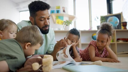 Group of small nursery school children with man teacher on floor indoors in classroom, reading book. - Powered by Adobe