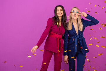 two attractive women celebrating new year on violet background in stylish colorful evening suits of purple and blue color, friends having fun together, fashion trend, golden confetti party mood
