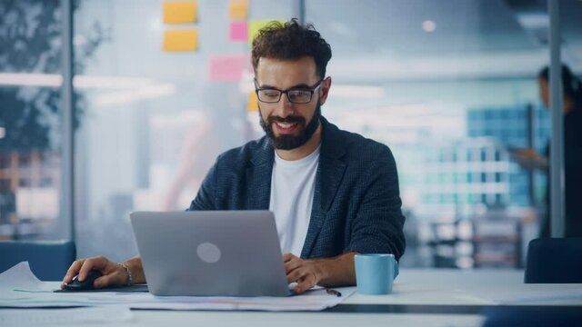 Modern Office: Portrait of Young Stylish Businessman Wearing Glasses Works on Laptop, Does Data Analysis, Website Design, Creative Developemnt. Digital Entrepreneur Works on e-Commerce Startup Project