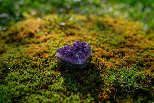 Beauterful purple ametist crystal close up on natural forest green moss background. Spiritual esoteric practice, magic healing rock for reiki crystal ritual.