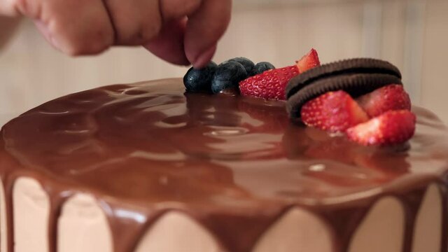 Woman Confectioner decorates chocolate cake with berries and cookies, close-up. Slow motion. Cake making process