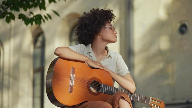 Sad female street musician holding acoustic guitar, looking around, no audience