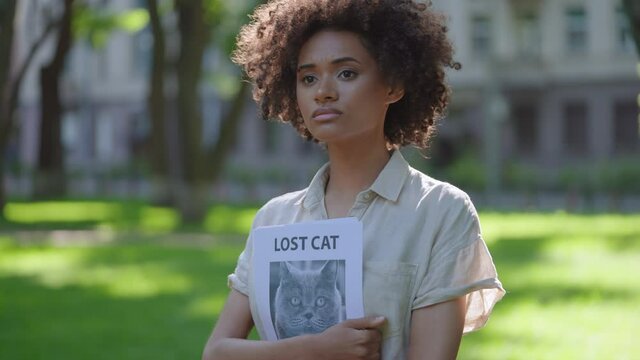 Upset curly haired woman holding missing cat poster, searching lost pet