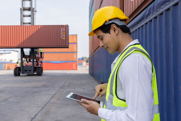 Engineer or foreman holding tablet and looking down to checking inventory or job details with cargo container background. Engineering site and working with technology concept.