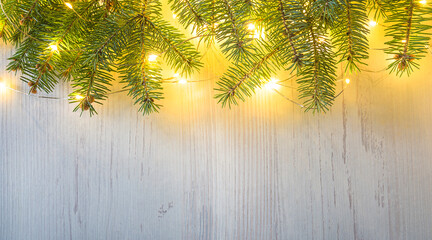 Framd of fir branches and christmas lights on white wooden background; space for text, flat lay