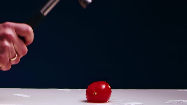 A man's hand hits a red tomato on a table with a hammer. Slow motion