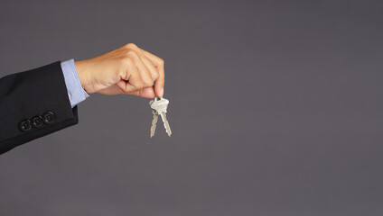 A businessman's hand holds a bunch of two keys over gray background with blank copy space for text message or information content